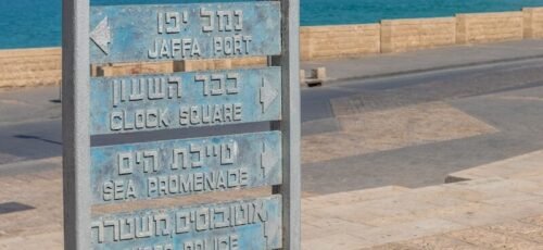 a sign in front of a body of water with a city in the background